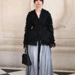 Mia Goth in a textured black Dior jacket and flowing gray trousers in Paris
